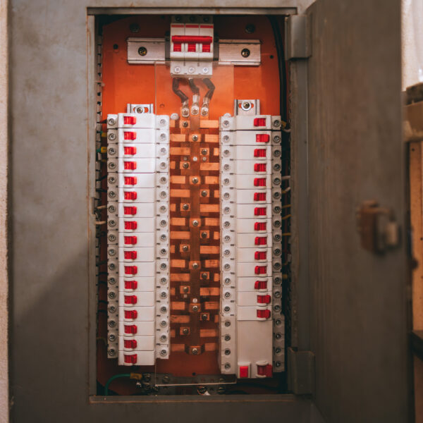 An open electrical panel with numerous circuit breakers and a neatly organized wiring system. The breakers have red switches and are arranged symmetrically on a metallic backing, in the panel box